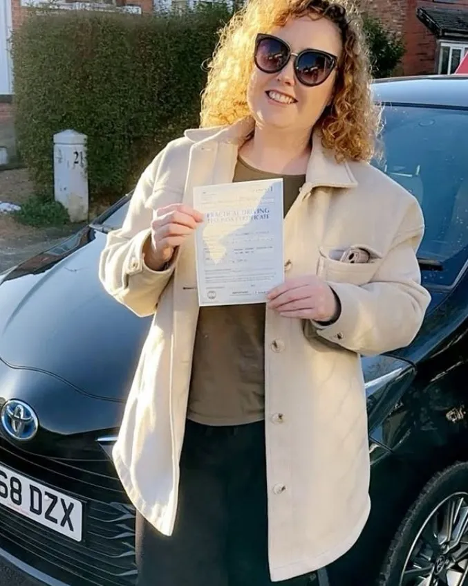 Alex with their pass certificate beside a Learn Local car